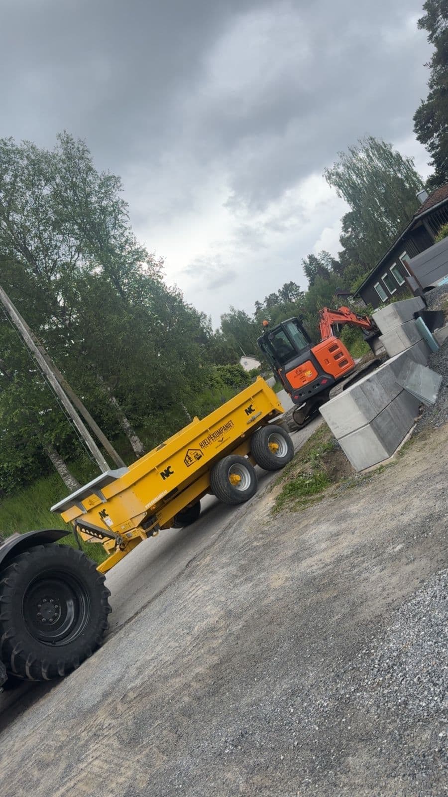 Gravemaskin og tipphenger ved en oppkjørsel med nye murblokker