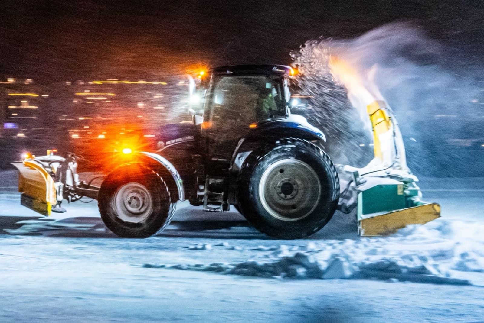 Traktor med brøyteskjær og snøfreser rydder snø om kvelden